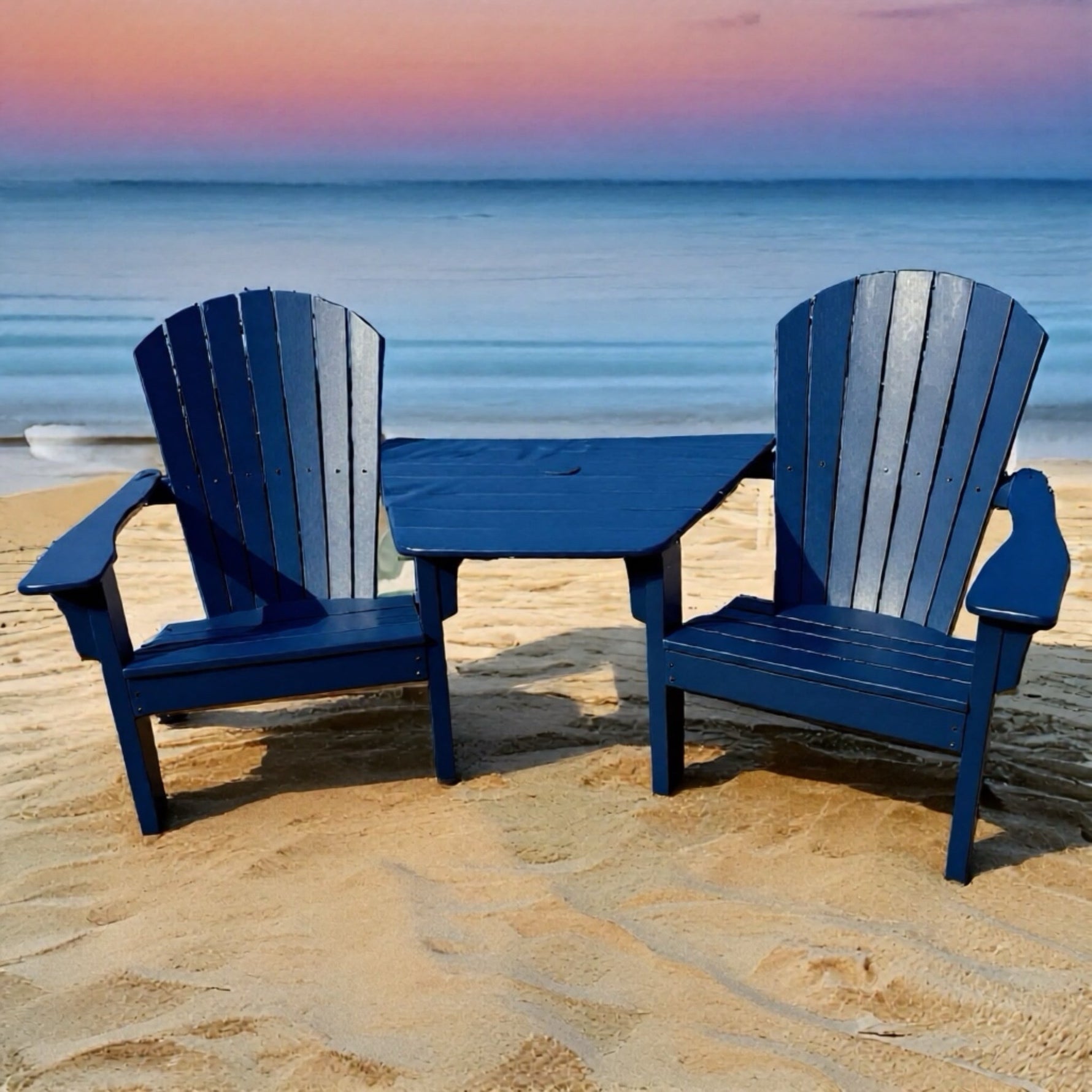 Two blue Adirondack chairs with a table on a sandy beach at sunset.