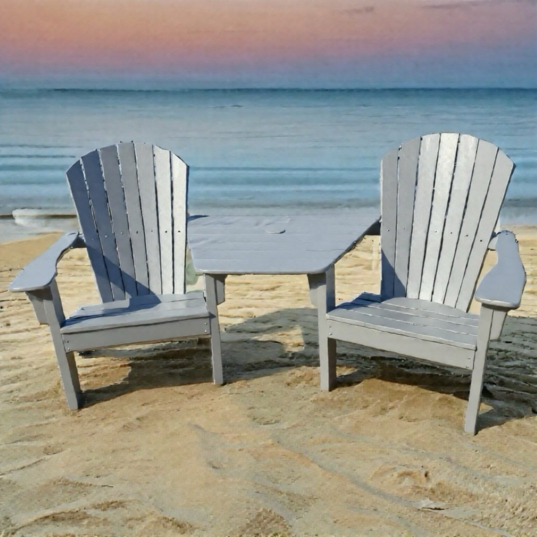 Two gray Adirondack chairs with a small  Tete table on a sandy beach.